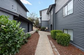 Burien apartment for rent - A concrete pathway leads between two buildings with green shrubbery on the sides.