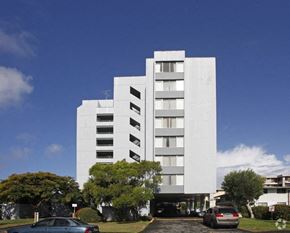 Honolulu apartment for rent - a tall white building with cars parked in front of it