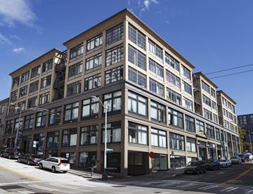 Seattle apartment for rent - A large building with many windows is situated on a street with cars parked on the side.