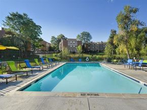 Denver apartment for rent - A swimming pool surrounded by chairs and trees with apartment buildings in the background.
