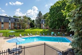 Battle Creek apartment for rent - A black fence surrounds a pool with chairs and umbrellas.