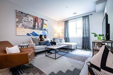 Detroit apartment for rent - A couple is sitting on a couch in a living room with a large painting on the wall.