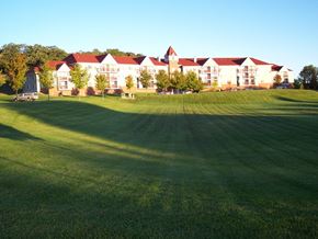 New Ulm apartment for rent - A large white building with a red roof sits in a grassy field.