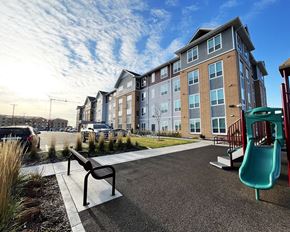 Forest Lake apartment for rent - A playground with a slide and a bench in front of a building.