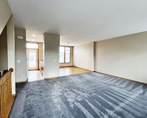 Faribault townhouse for rent - A spacious room with a blue carpet and wooden railings.
