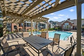 Olathe apartment for rent - A wooden pergola over a table with chairs and a pool in the background. at Somerset Oaks Apartment Homes, Olathe 66062