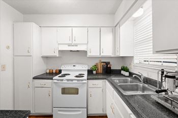 A white kitchen with a black countertop and a stove top oven.