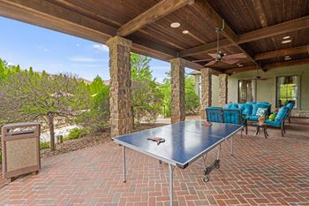A table is on a patio with a blue couch and a fan.