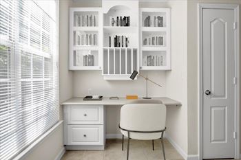A white desk with a chair and a bookshelf with books.