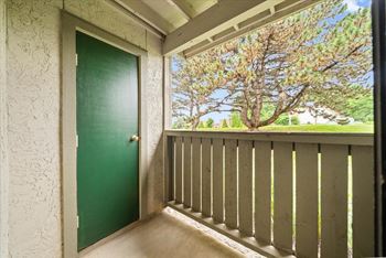 A green door is on the left of a balcony with a view of trees.