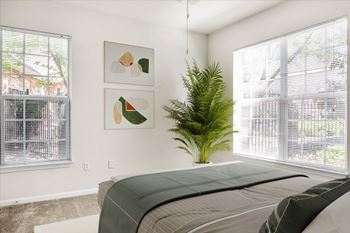 A bedroom with a bed, a plant, and two framed pictures on the wall.