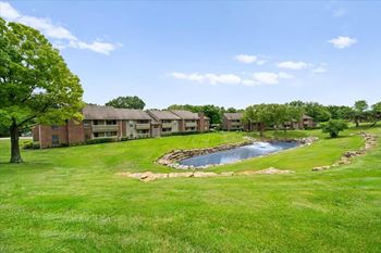 A small pond in the middle of a grassy area with a building in the background.