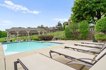 A pool with sun loungers and a pavilion in the background.
