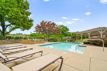 A pool surrounded by trees and chairs.