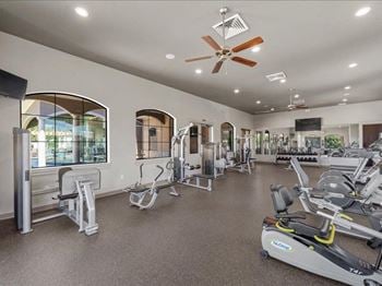 A gym with various exercise machines and a ceiling fan