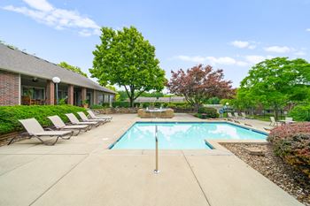A pool surrounded by trees and chairs in front of a house.