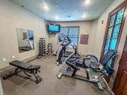 Kansas City apartment for rent - Compact fitness center at The Dorset Apartments featuring cardio machines, weight bench, dumbbells, and a mounted TV.