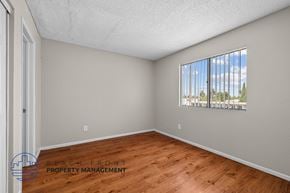 Long Beach apartment for rent - A room with wooden flooring and a window showing a view of trees and a building.
