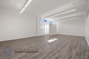 Long Beach apartment for rent - A spacious room with wooden flooring and white walls, with a logo for Beach Front Property Management in the bottom left corner.