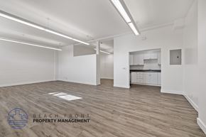 Long Beach apartment for rent - A spacious room with wooden flooring and white walls, with a logo for Beach Front Property Management in the bottom left corner.