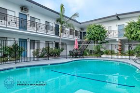 Long Beach apartment for rent - A swimming pool is surrounded by a black fence and a building with balconies.