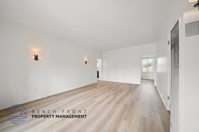 Riverside apartment for rent - A spacious room with wooden flooring and white walls, with a logo for Beach Front Property Management in the bottom left corner.