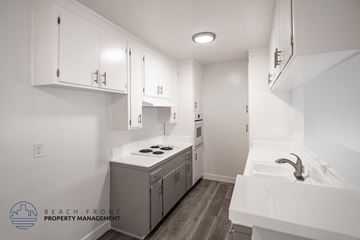 Long Beach apartment for rent - A clean, white kitchen with wooden floors and a logo for Beach Front Property Management.