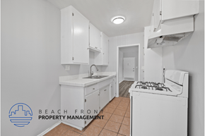Long Beach apartment for rent - A kitchen with white cabinets and appliances, with a logo for Beach Front Property Management in the bottom left corner.