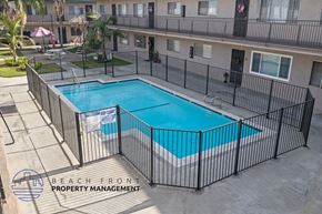 Downey apartment for rent - A pool surrounded by a black fence with the words Beach Front Property Management on it.