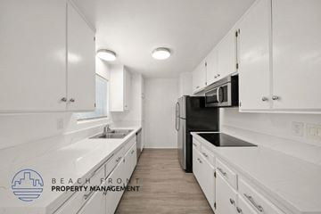 Santa Monica apartment for rent - A kitchen with white cabinets and appliances, with a logo for Beach Front Property Management in the bottom left corner.