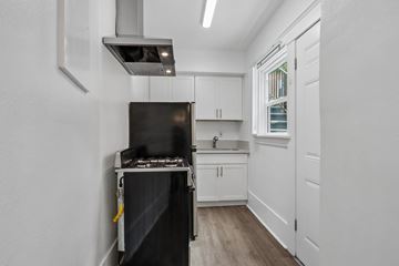 Long Beach apartment for rent - A black stove is in a white kitchen with wood floors.