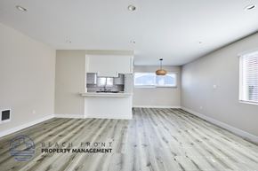 Redondo Beach apartment for rent - A spacious room with wooden flooring and a logo for Beach Front Property Management in the corner.