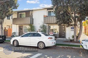 Long Beach apartment for rent - A white car is parked in front of a two-story building with a sign that reads "BEACH FRONT PROPERTY MANAGEMENT.".