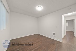 Redondo Beach apartment for rent - A spacious room with wooden flooring and white walls, with a logo for Beach Front Property Management in the bottom left corner.