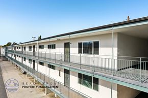 Lomita apartment for rent - A row of white buildings with balconies and the logo of Beachfront Property Management in the bottom left corner.