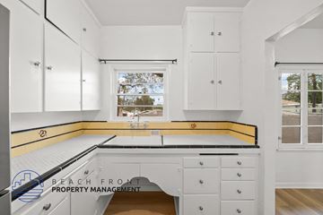 Riverside apartment for rent - A kitchen with white cabinets and a window overlooking a beach.