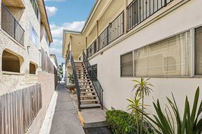 San Pedro apartment for rent - A narrow street with a wooden fence on the left and a white building on the right.