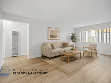 Downey apartment for rent - A living room with a couch, chair, and a rug with the words "Beach Front Property Management" on the bottom left.