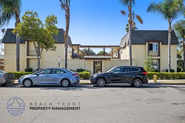 Anaheim apartment for rent - Two cars parked in front of a building with the logo "BEACH FRONT PROPERTY MANAGEMENT" on the ground.