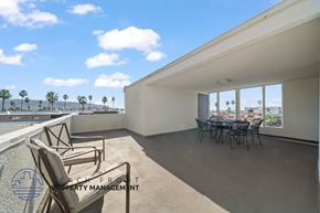 Redondo Beach apartment for rent - A balcony with chairs and a table is overlooking a pool and palm trees.