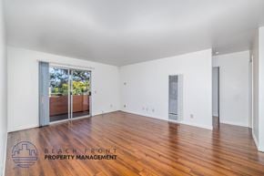 Long Beach apartment for rent - A spacious room with wooden floors and white walls, with a view of a balcony outside.