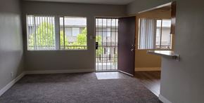 Downey apartment for rent - A room with a carpeted floor, a sliding door, and a window with a view of a fence and trees.