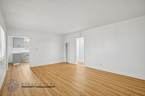San Pedro apartment for rent - A spacious room with wooden flooring and white walls, with a logo for Beach Front Property Management in the bottom left corner.
