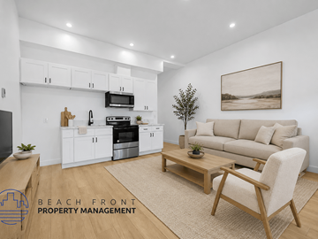 Long Beach apartment for rent - A modern kitchen with white cabinets and appliances, a wooden coffee table, and a beige sofa with a painting on the wall.