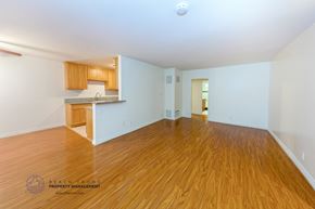 Los Angeles apartment for rent - A spacious room with wooden flooring and a kitchen area in the background.