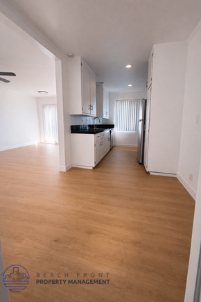 Long Beach apartment for rent - A spacious, empty room with wooden floors and white walls, with a kitchen area visible in the background.