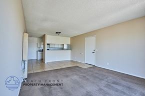 Long Beach apartment for rent - A spacious room with a carpeted floor and a logo for Beach Front Property Management in the bottom left corner.