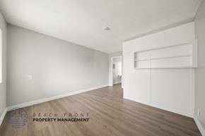 Hawthorne apartment for rent - A spacious room with wooden flooring and white walls, with a logo for Beach Front Property Management in the bottom left corner.