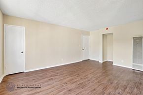 Redondo Beach apartment for rent - A spacious room with wooden flooring and white walls, with a door on the left and a window with a screen on the right.