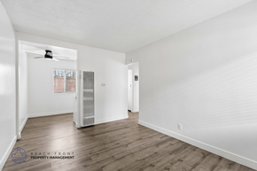 Hawthorne apartment for rent - A spacious room with wooden floors and white walls, featuring a ceiling fan and a window with blinds.